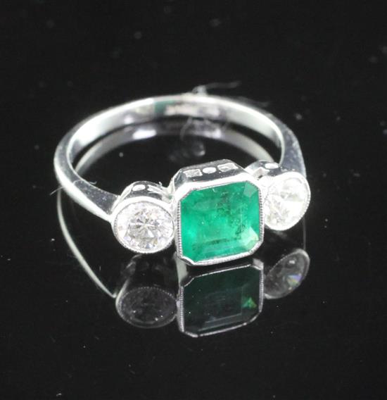 An 18ct white gold and three stone emerald and diamond ring, size L.